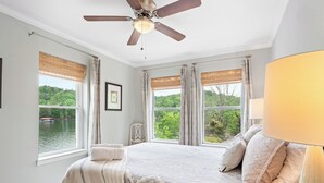 A bedroom with a large bed, a ceiling fan, and a view of a lake through the windows.