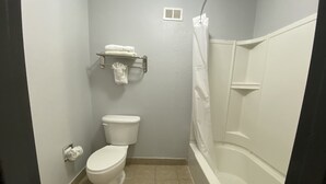 A bathroom with a toilet, a towel rack with towels, a shower curtain, and a toilet paper holder. - Quality Inn Alice (Alice)