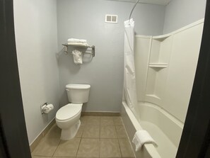 Een badkamer met toilet, een handdoekrek met handdoeken, een douchegordijn en een toiletpapierhouder.