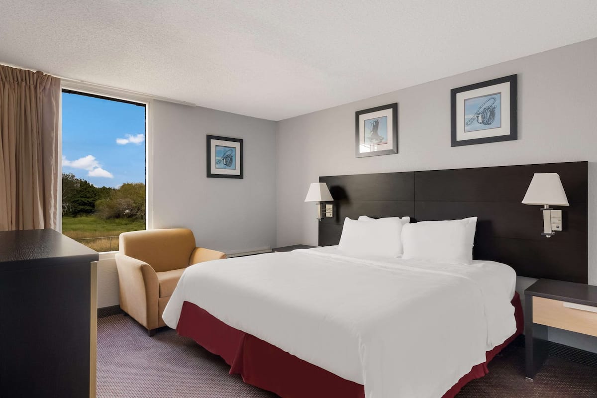 A hotel room with a large bed, a chair, a desk, and a window with a view of the outdoors.
