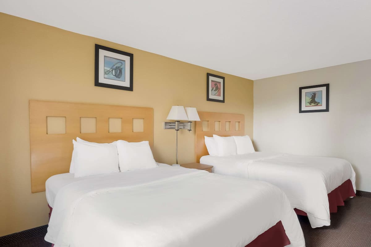 A hotel room with two beds, a nightstand, and a lamp.