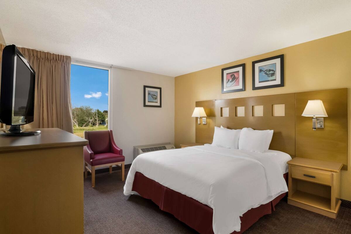A hotel room with a large bed, a desk with a TV, a chair, and two bedside lamps.