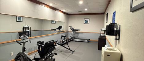 Un gimnasio con equipamiento de ejercicio, un espejo y un refrigerador.