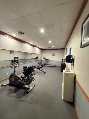 A gym with exercise equipment, a mirror, and a refrigerator. - Alice Western Inn (Alice)