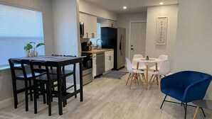 A modern kitchen with white cabinets, a dining area with a black table and chairs, and a blue chair.