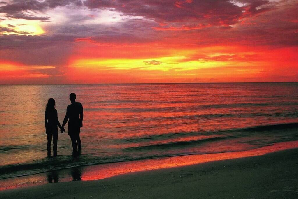Solnedgang over havet med to silhuetfigurer, der holder hånd på stranden.