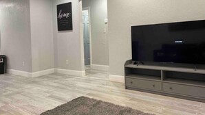 A living room with a flat-screen TV on a stand, a rug, and a 'home' sign on the wall.