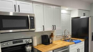 A modern kitchen with white cabinets, stainless steel appliances, a wooden countertop, and a built-in dishwasher.