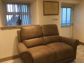 Un fauteuil en cuir marron se trouve dans une pièce dotée d’une fenêtre, d’un tableau au mur et d’un thermostat.
