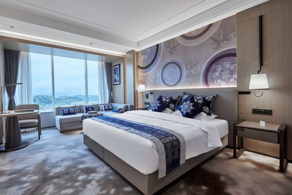 Ett modernt hotellrum med en stor säng, en soffa, ett skrivbord och utsikt över bergen.