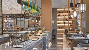 A modern restaurant with a long counter, various food stations, and a decorative chandelier. - Howard Johnson by Wyndham Tianxiaqiguan Hotel Xingwen (Yibin)