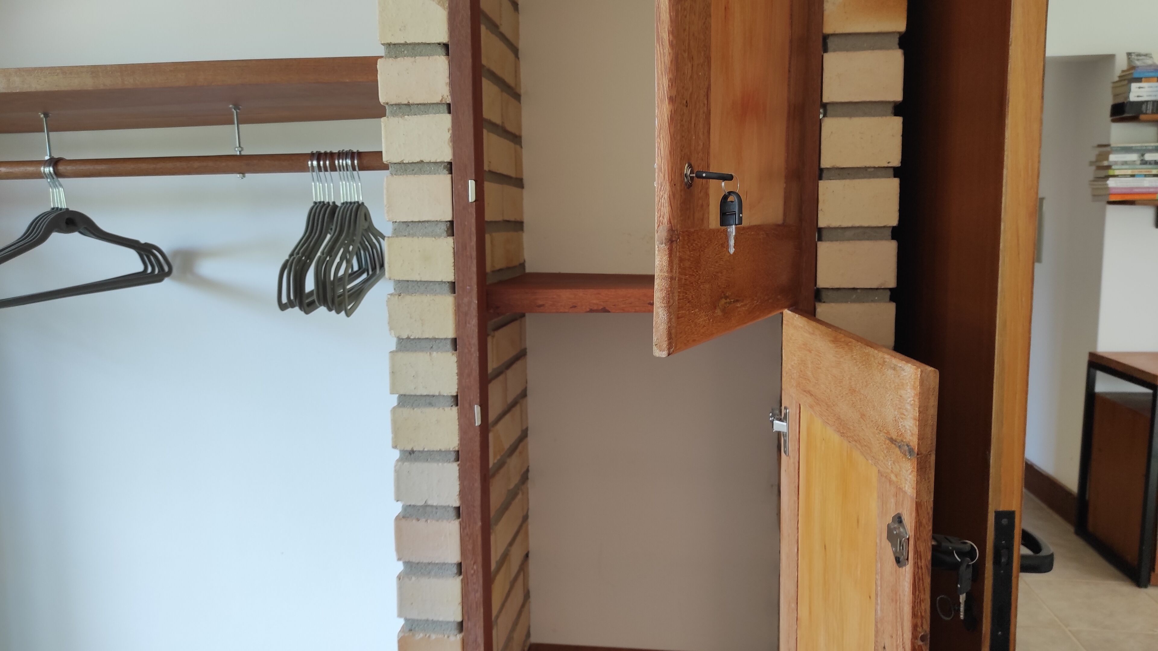 A room with a wooden door, a brick wall, and a wooden shelf with hangers.