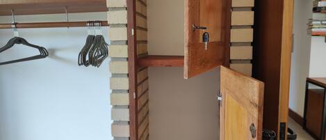 A room with a wooden door, a brick wall, and a wooden shelf with hangers.