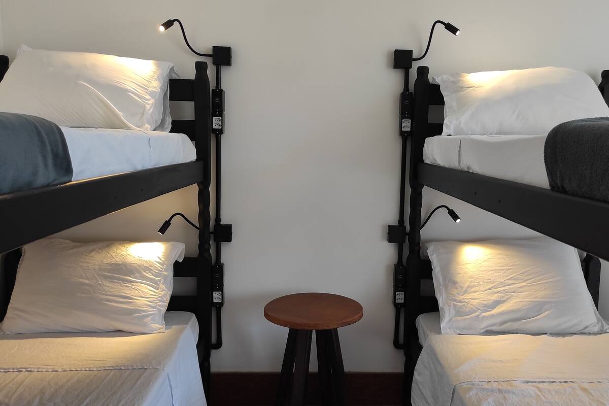 Une chambre avec deux lits superposés, chacun doté d’une table de chevet et d’une lampe, et un petit tabouret au centre.
