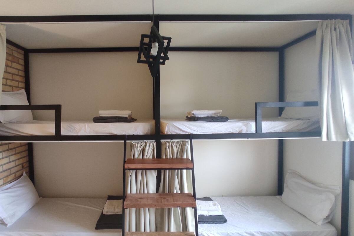 Une chambre avec un lit superposé, une échelle en bois, du linge de lit blanc et des rideaux.