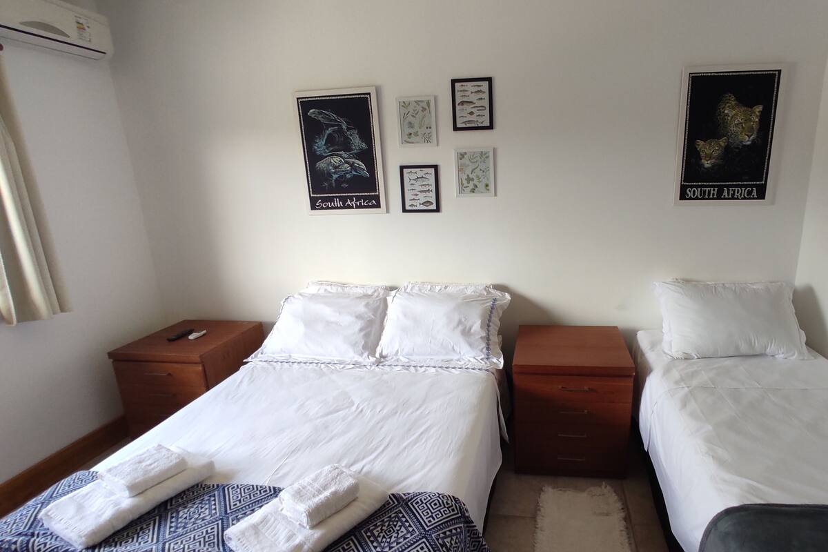 Une chambre d’hôtel avec deux lits simples, une table de chevet en bois et un climatiseur fixé au mur.