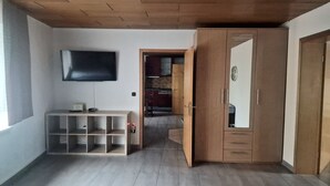 A room with a wooden ceiling, a TV mounted on the wall, a desk with a computer, and a wardrobe with a mirror. - W.I.L.A. 1 (Helmbrechts)