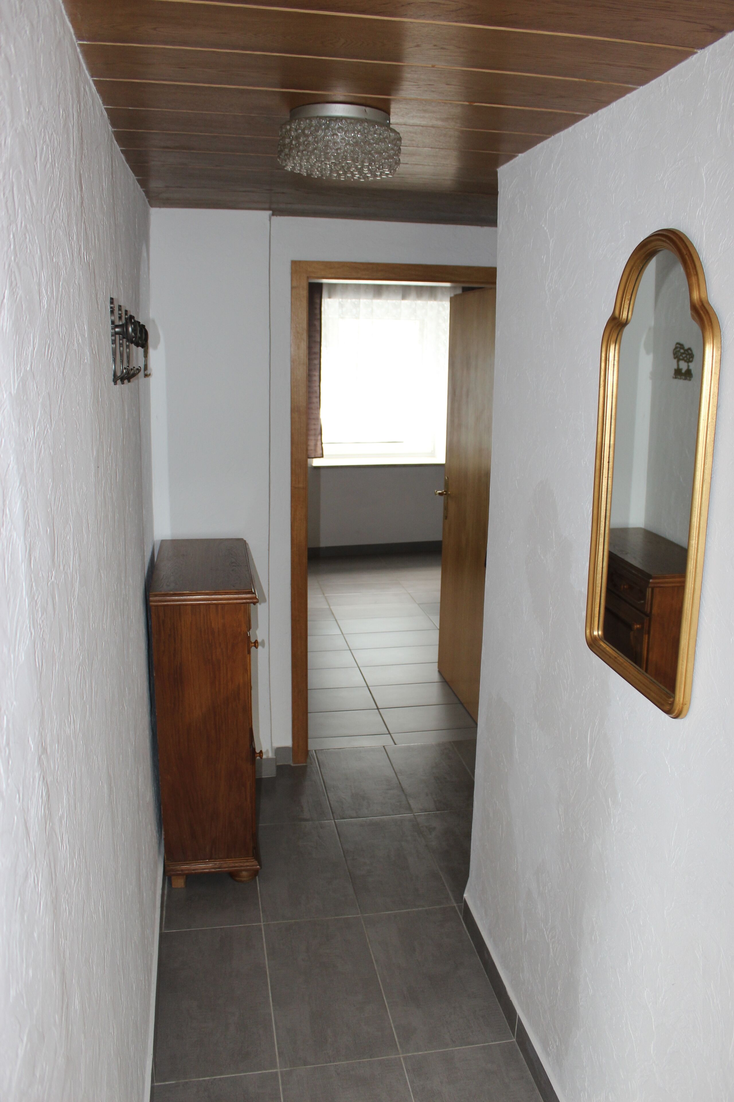 Um corredor com um armário de madeira, um espelho e uma porta que dá para outro cômodo.