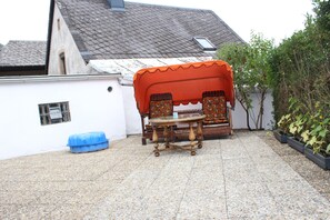 An outdoor seating area with a table and chairs, a blue plastic tub, and a white wall with a window. - W.I.L.A. 1 (Helmbrechts)