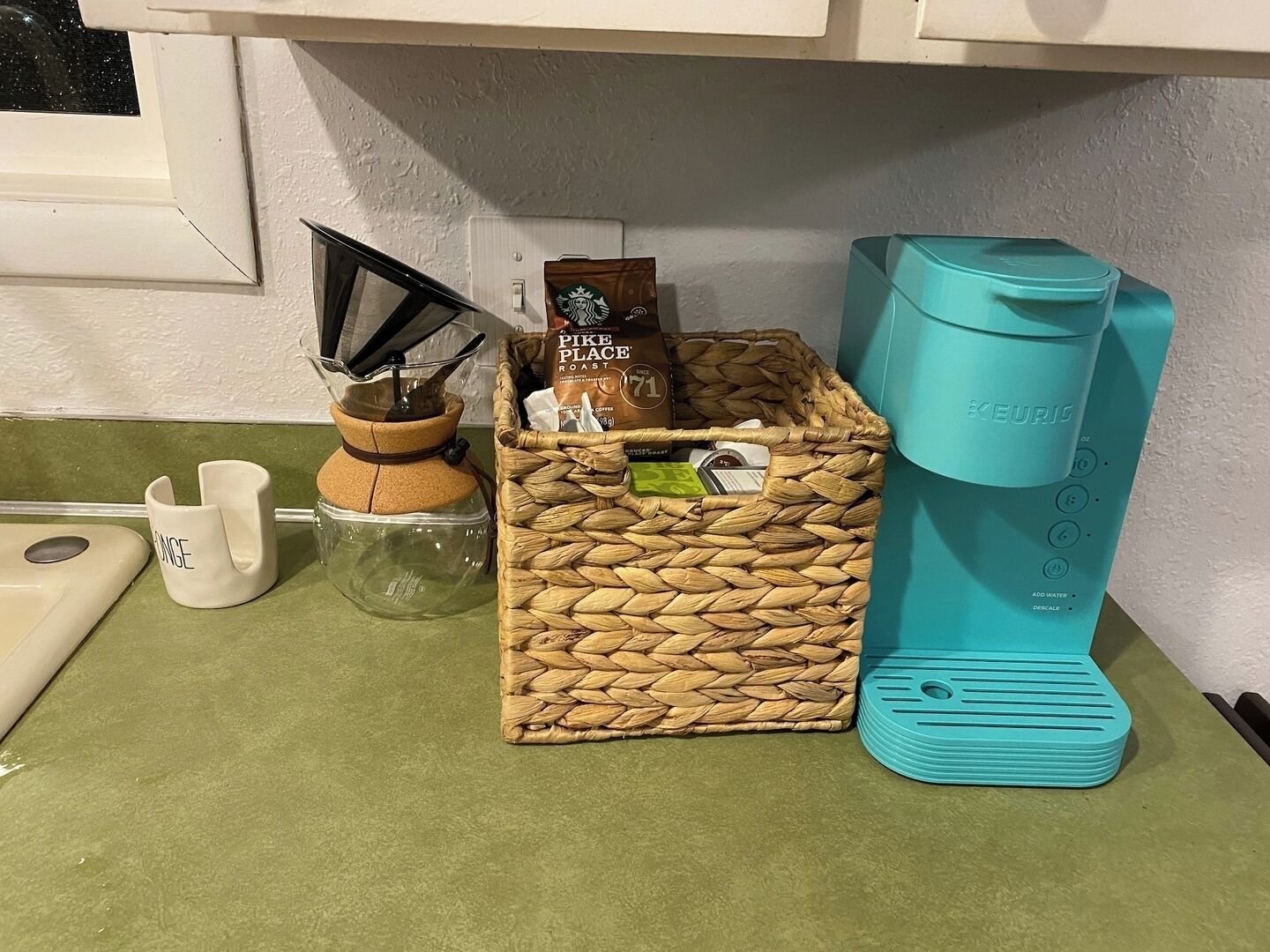 Eine Küchenarbeitsplatte mit einer Kaffeemaschine, einem gewebten Korb voller Kapseln, einer Kaffeemühle und einer Tasse.