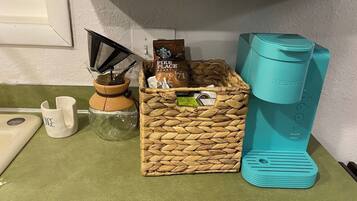 Eine Küchenarbeitsplatte mit einer Kaffeemaschine, einem gewebten Korb voller Kapseln, einer Kaffeemühle und einer Tasse.