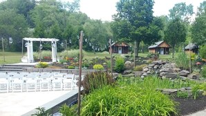 A garden with a pergola, white chairs, and rustic cabins.
