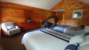 A cozy log cabin room with a large bed, a wooden dresser, a chair, and a desk with a table.