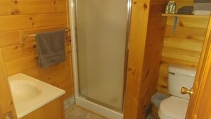 A wooden cabin bathroom with a shower, toilet, and sink.