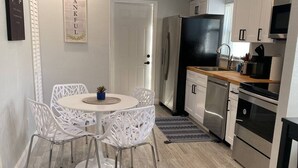 A modern kitchen with white cabinetry, a black refrigerator, stainless steel appliances, and a dining area with white chairs and a small table.