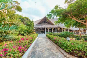 A pathway leading to a thatched-roof structure surrounded by lush greenery and vibrant flowers.