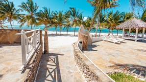 Un resort frente al mar con un camino de piedra que lleva a una zona de estar con sillones y una estructura de techo de paja.
