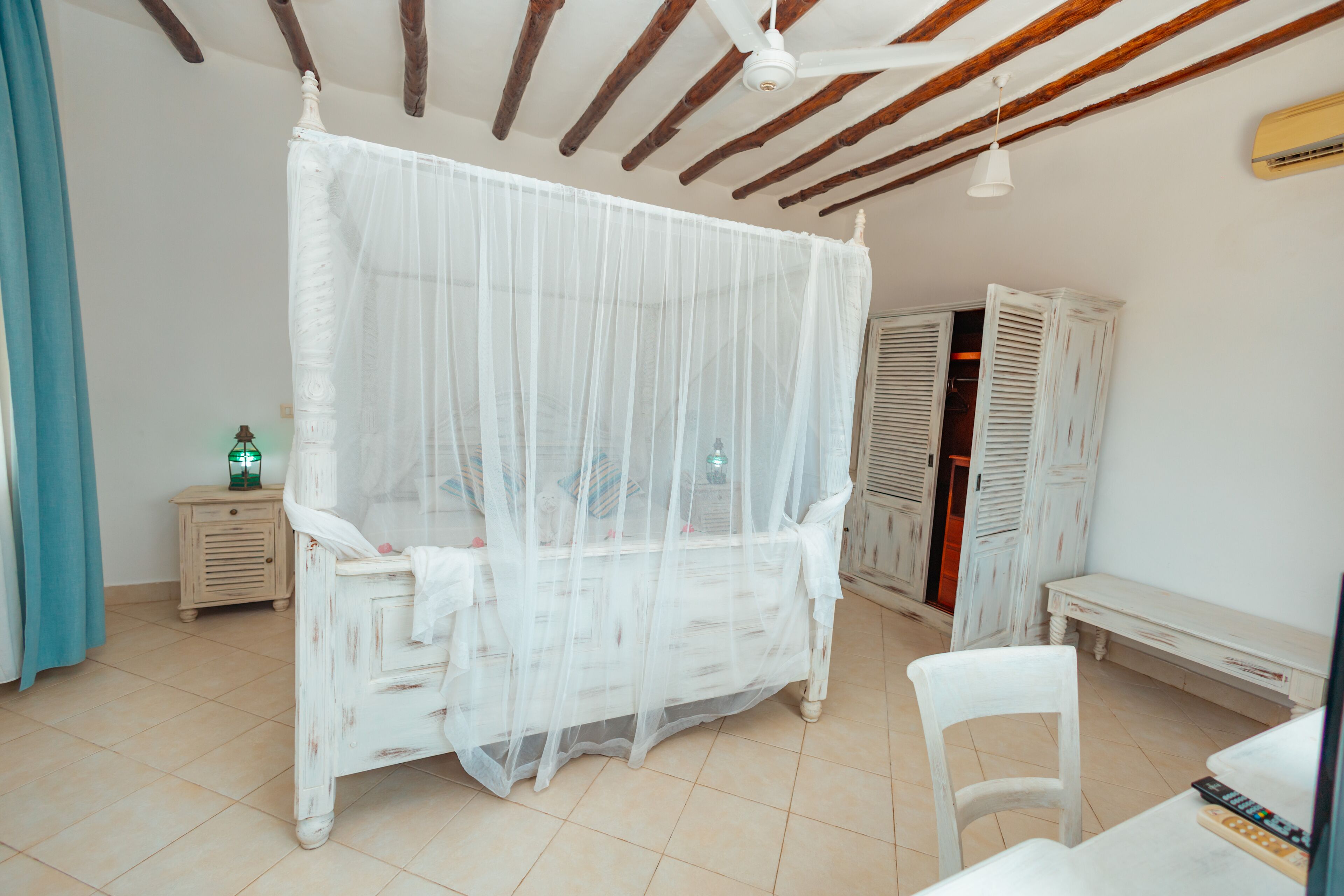Un dormitorio con cama con dosel, una mesita de noche, una silla y un armario.