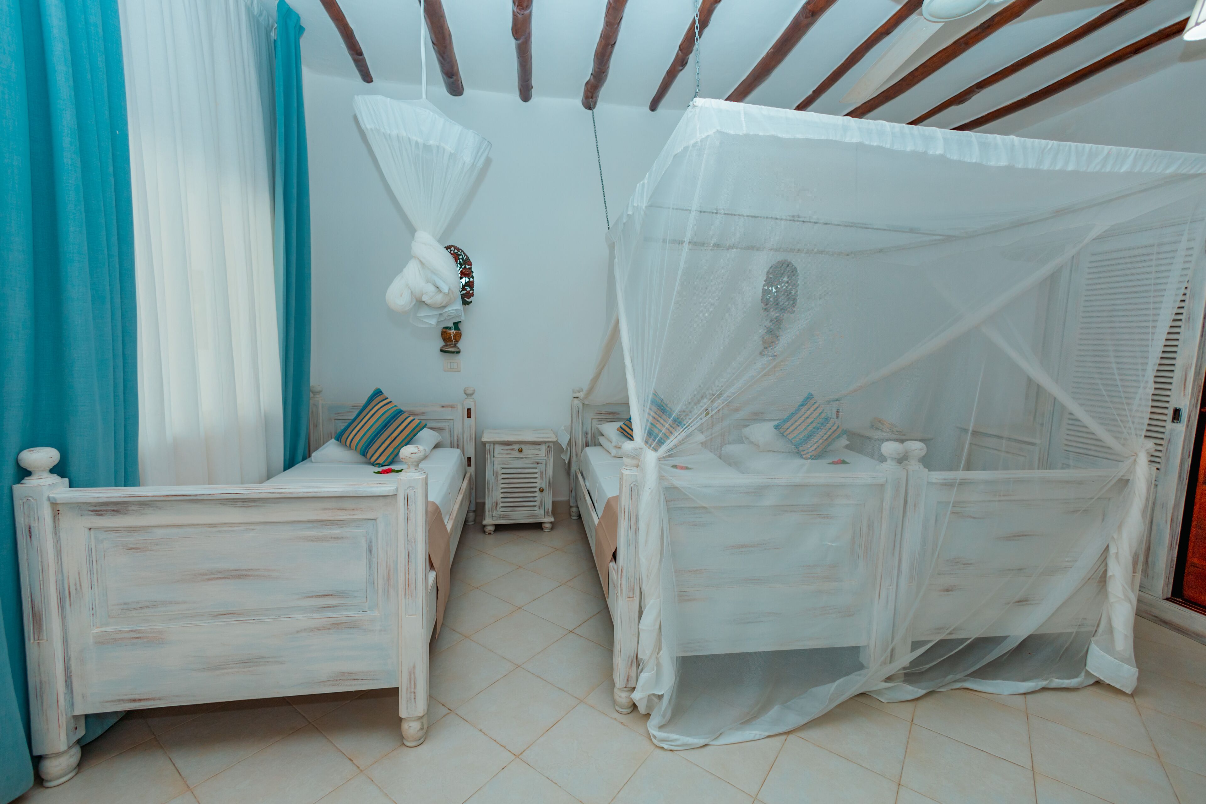 Une chambre à coucher avec deux lits simples, chacun doté d’un baldaquin. On y trouve une petite table de chevet avec une lampe, ainsi qu’un objet décoratif accroché au mur.