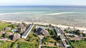 Vista aérea de un resort con edificios de techo de paja, una piscina y una playa.