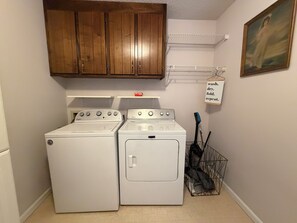 Une buanderie équipée d’un lave-linge et d’un sèche-linge, de placards en bois, d’une étagère en métal et d’un panneau indiquant les instructions de lavage.