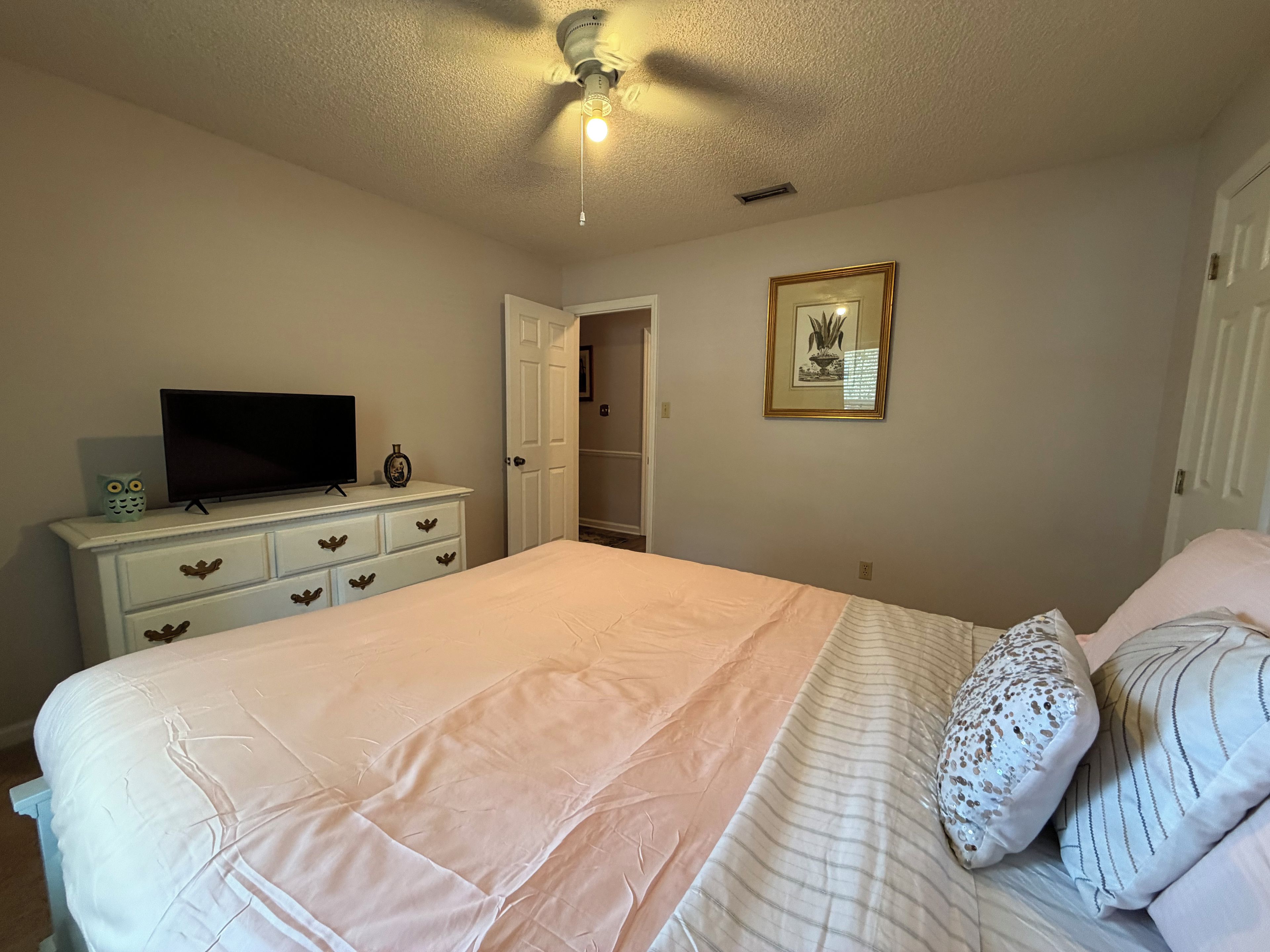 A bedroom with a bed, dresser, television, and a ceiling fan.