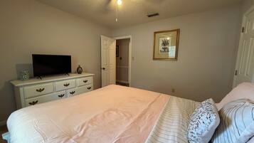 A bedroom with a bed, dresser, television, and a ceiling fan.
