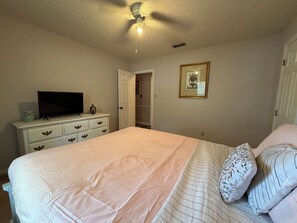 Een slaapkamer met een bed, een dressoir, een televisie en een plafondventilator.