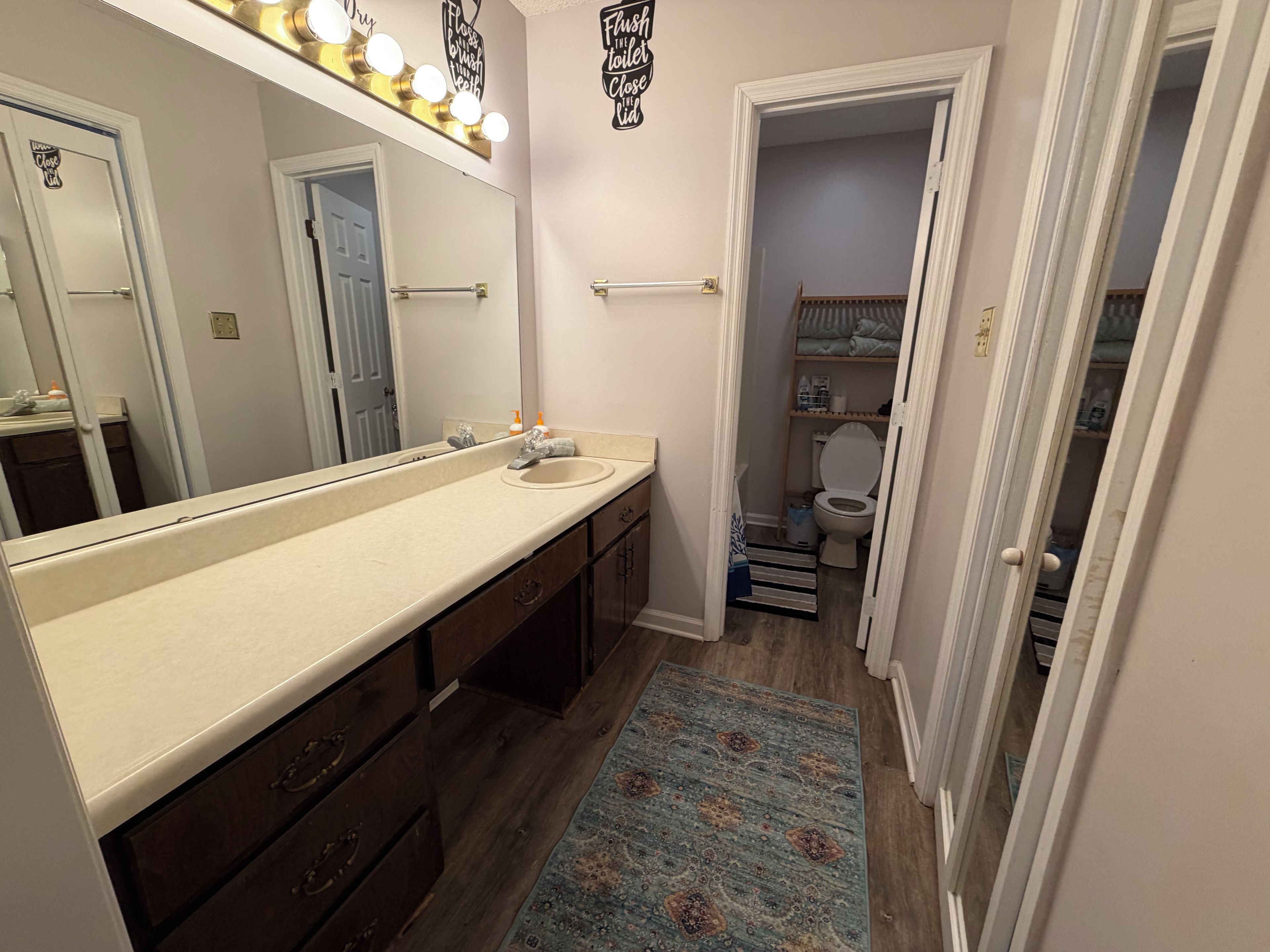 A bathroom with a large mirror, vanity, and a toilet visible through an open door.