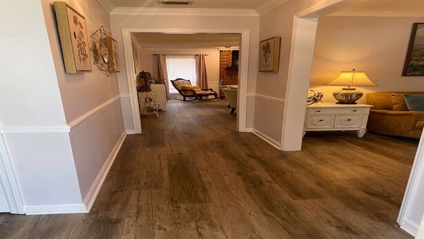 Ein Flur mit Holzboden, der in einen Wohnbereich mit Sofa und Lampe führt.