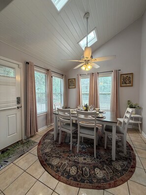 Un coin repas avec une table ronde, des chaises blanches, un ventilateur de plafond et un tapis à motifs.