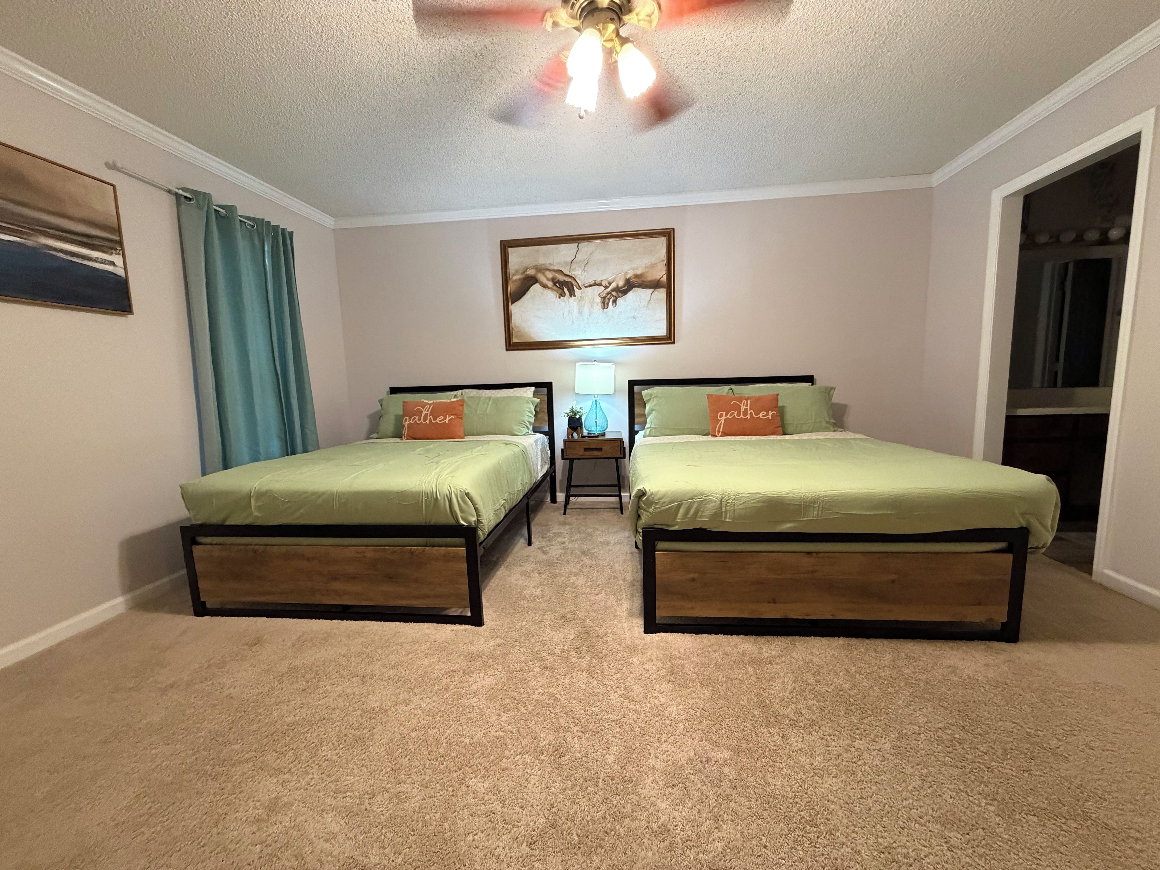 A bedroom with two beds, a ceiling fan, a painting, and a nightstand with a lamp.