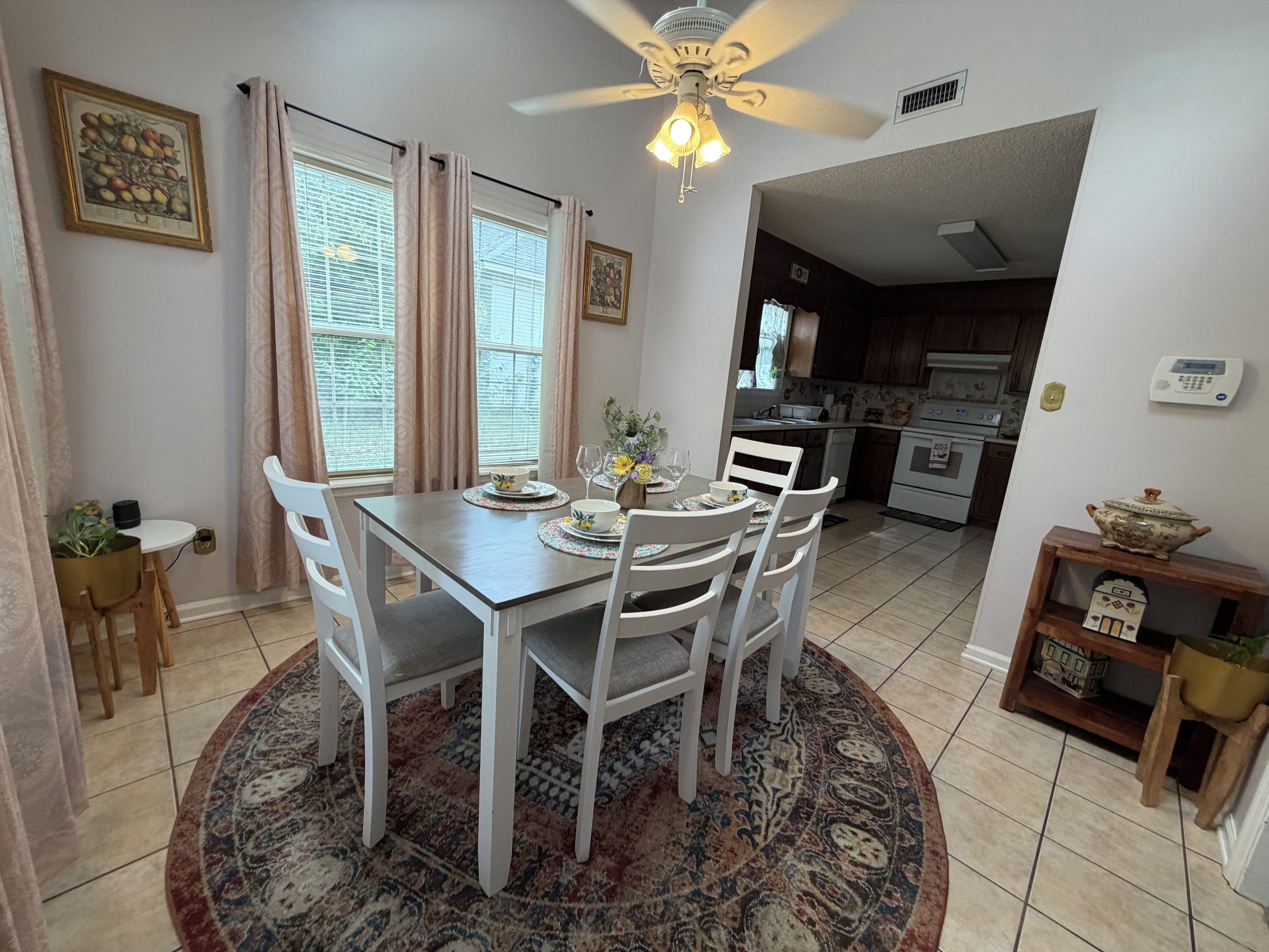 Un comedor con una mesa dispuesta para cuatro personas, un ventilador de techo y una cocina al fondo.