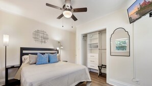 Une chambre à coucher comprenant un lit, un ventilateur de plafond, une armoire et un téléviseur fixé au mur.