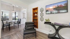Una sala de estar moderna con comedor, un sillón de cuero negro, una estantería de madera y un televisor montado en la pared.