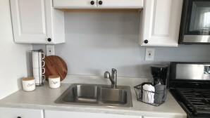 Cuina amb armaris blancs, un rentapeus d'acer inoxidable, una cafetera i una torradora.