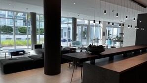 Un interior moderno con una larga recepción, área de descanso y ventanas amplias que ofrecen vistas al exterior.