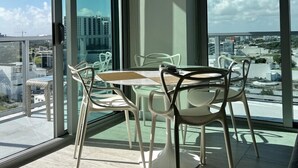 Un balcón con mesa y sillas, ventanas amplias y vista a la ciudad.