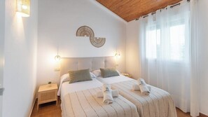 Une chambre double avec deux lits, un plafond en bois et une grande fenêtre ornée de rideaux légers.