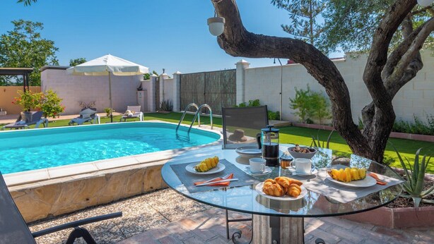 A glass table with breakfast items, a pool, and a tree in a backyard setting. - El Reposo Alhaurín de la Torre by Ruralidays (Málaga)